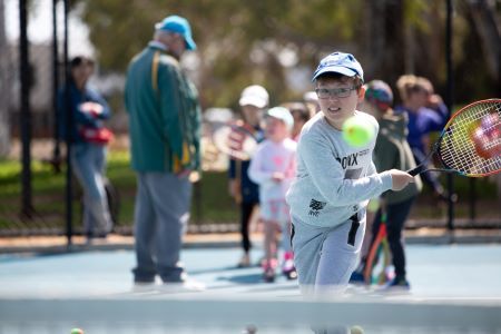 Child playing tennis with other players in background