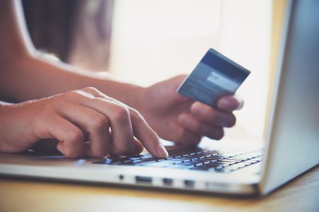 Person's hands holding credit card near a computer