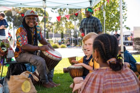 Smiling man playing hand drums, surrounded by children