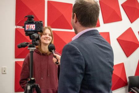 Young person speaking into a microphone behind a camera