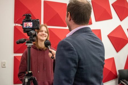 Young person speaking into a microphone behind a camera