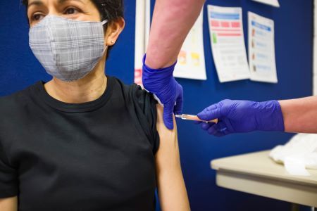 Womanwaring a mask receiving injection into left arm